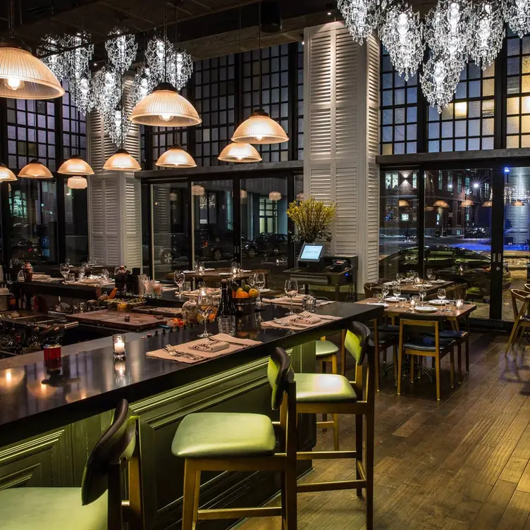 A dining room with wooden floors and high ceilings, and a bar on the left side with green leather stools at Jellyfish Restaurant, one of the best special occasions restaurants in Montreal