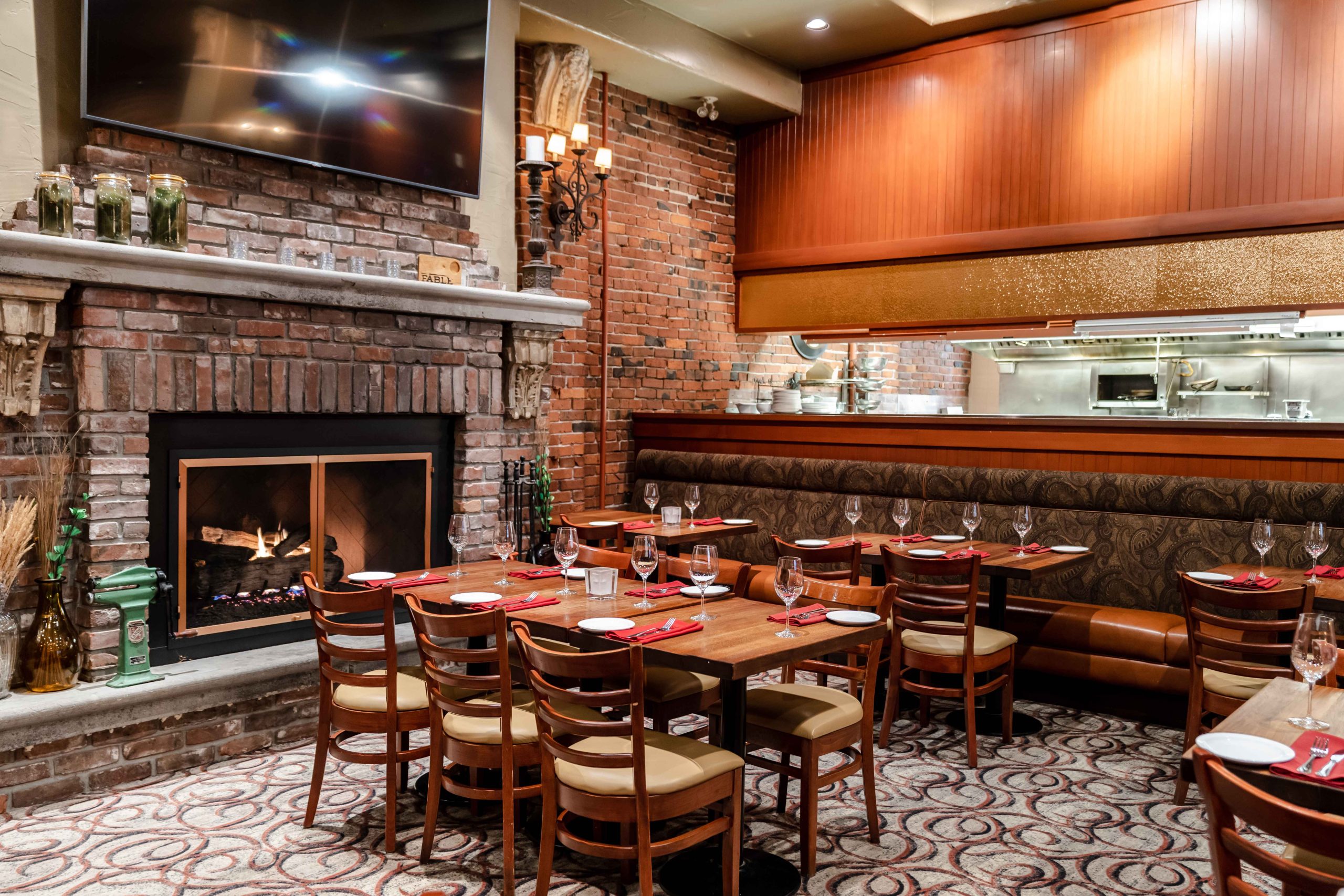 A restaurant with brick walls, wooden tables, a big fireplace and a wooden counter