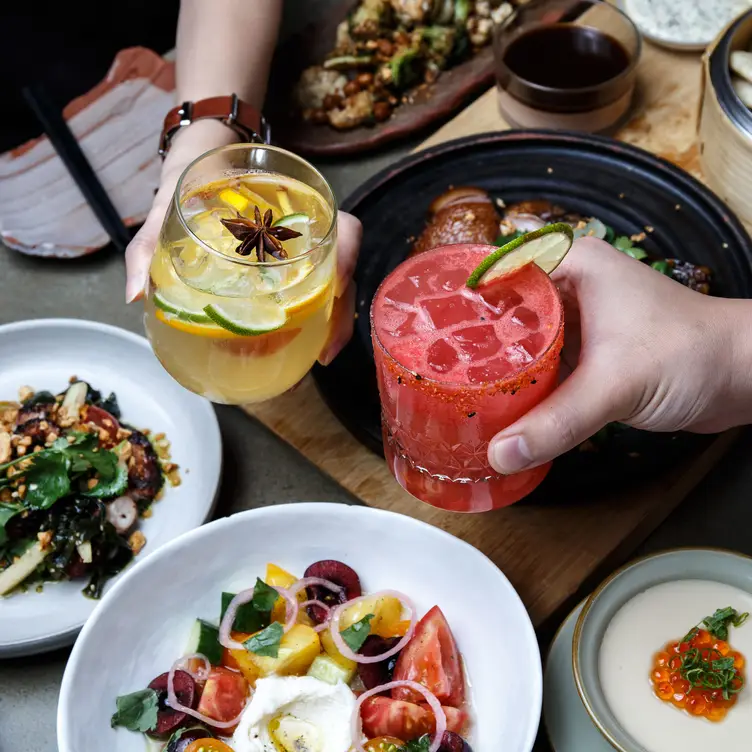 Two diners toasting with colourful cocktails and Asian plates at Torafuku, one of the best first date restaurants in Vancouver.