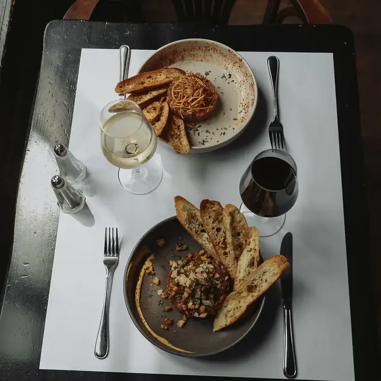 A table featuring two tartare dishes and a glass of white and red wine at Modavie, one of the best romantic restaurants in Montreal for dates