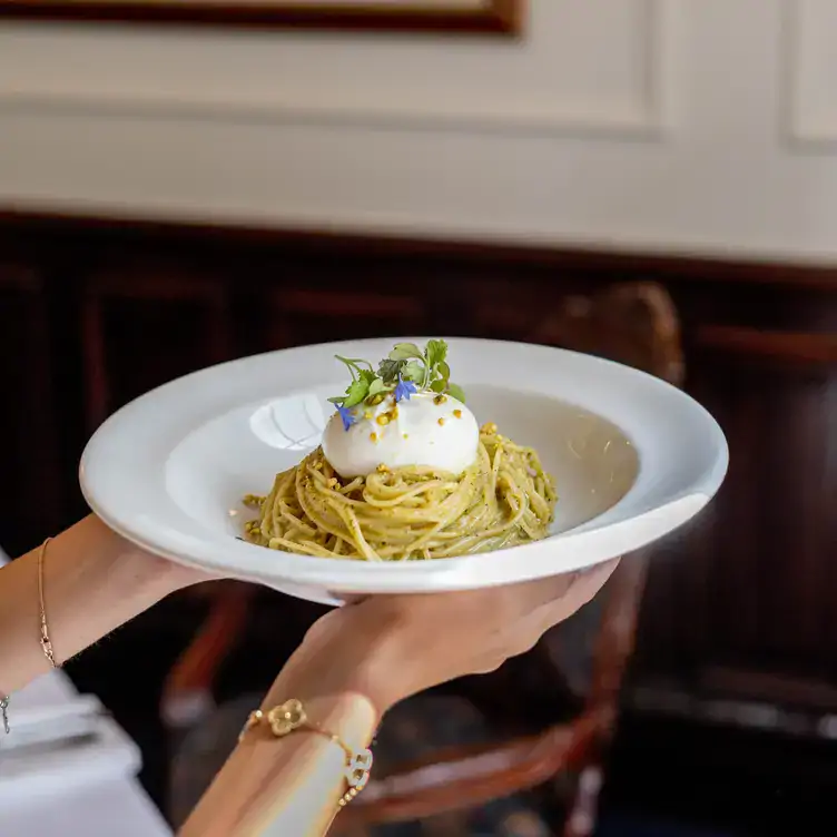 A waitress holds a bowl of pesto spaghetti pasta topped with burrata at Le Muscadin, one of the best Italian restaurants in Old Montreal