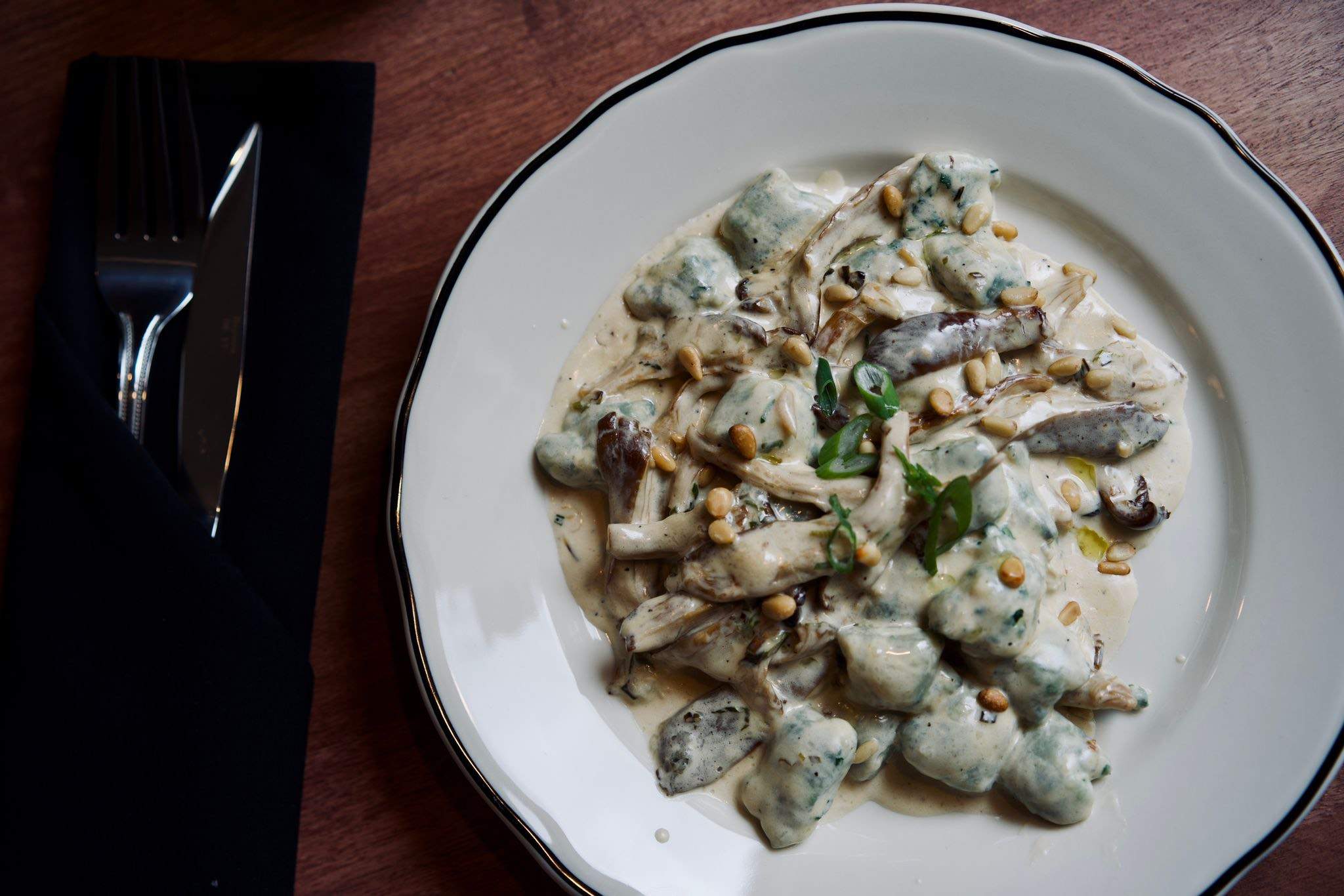 A gnocchi dish with a cream sauce and mushrooms in a white plate on a table