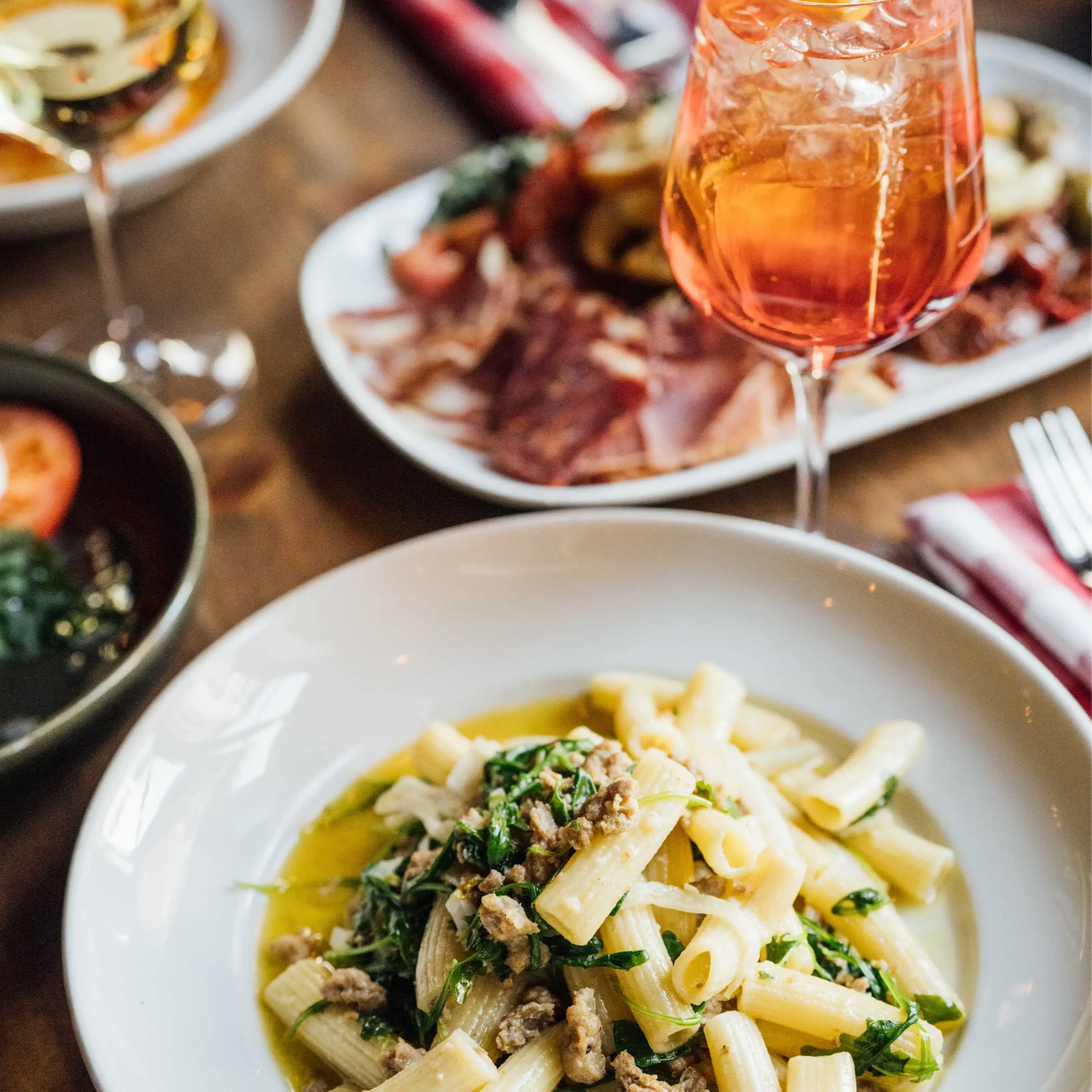 A bowl of white rigatoni pasta with spinach next to a glass of Aperol spritz and Italian antipasti at BEVO Bar + Pizzeria, one of the best Italian restaurants in Old Montreal