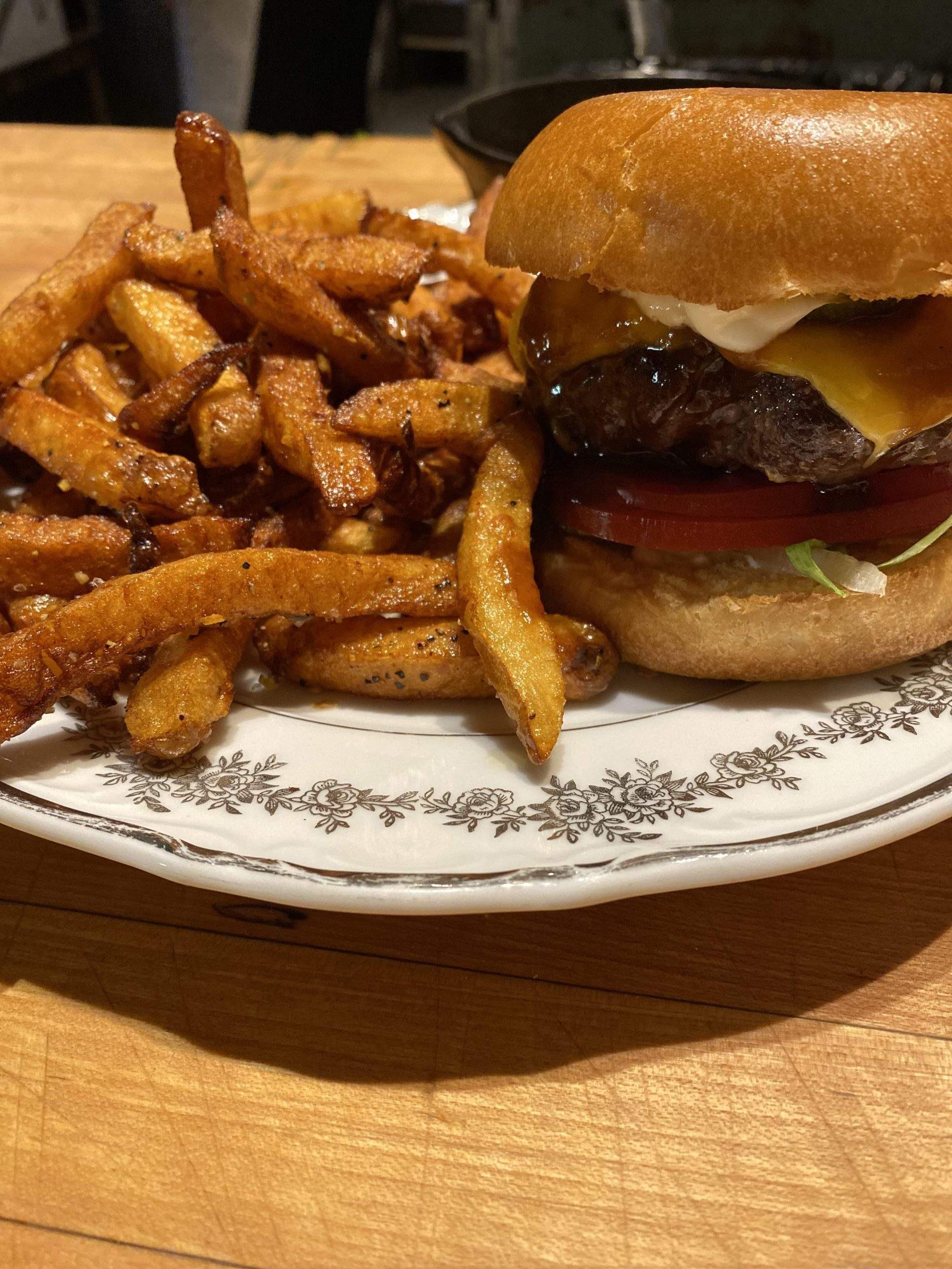 A burger with a side of fries on a white plate on a wooden table