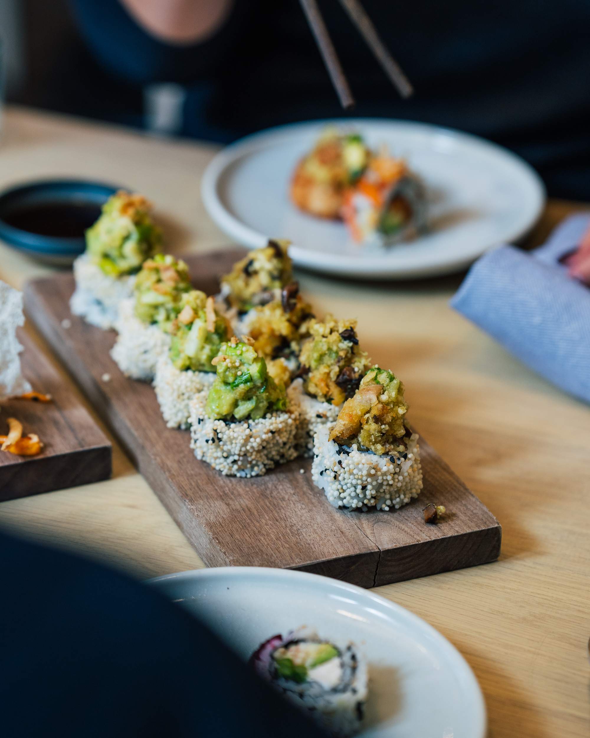 A wooden board with a range of white and green sushis on a restaurant table.