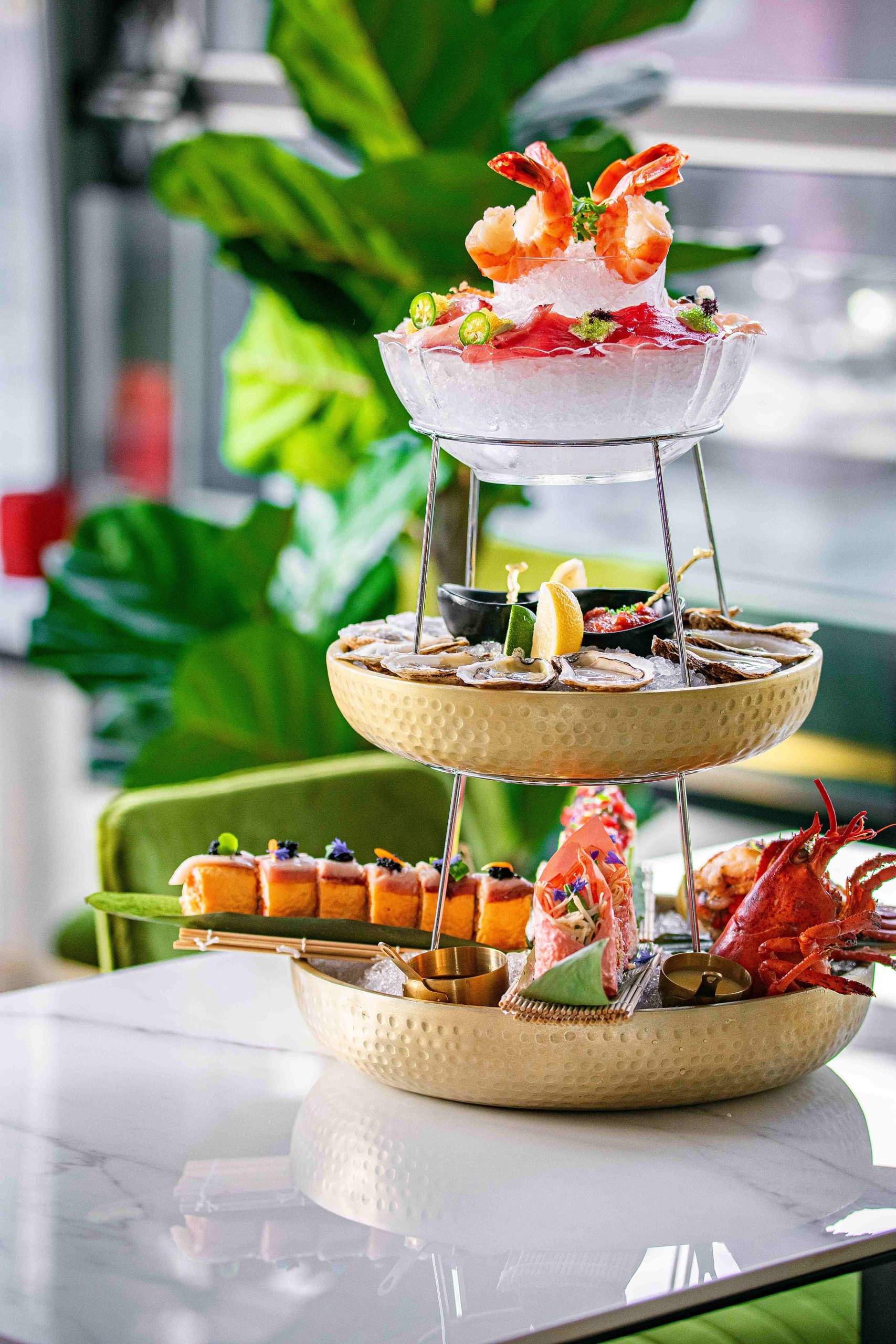 A seafood tower features an array of seafood and raw fish over three plates at a restaurant.