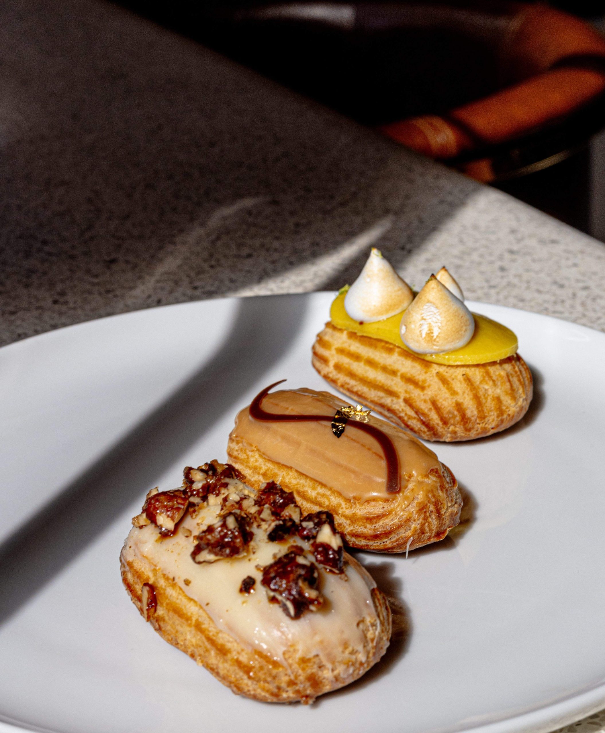 Three small éclair pastries with lemon, caramel and vanilla fillings on a white plate.