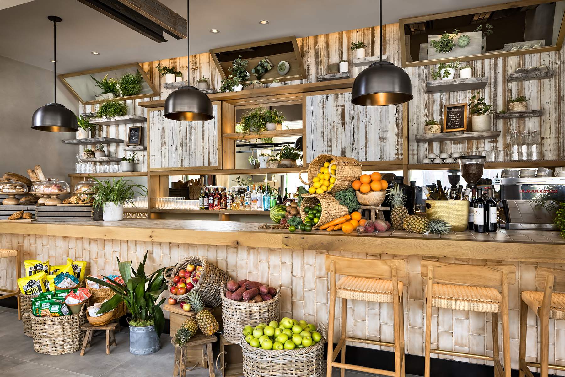 Le comptoir d'un restaurant avec des paniers de fruits, des tabourets en bois, un coin pâtisserie et des bouteilles alignées au mur