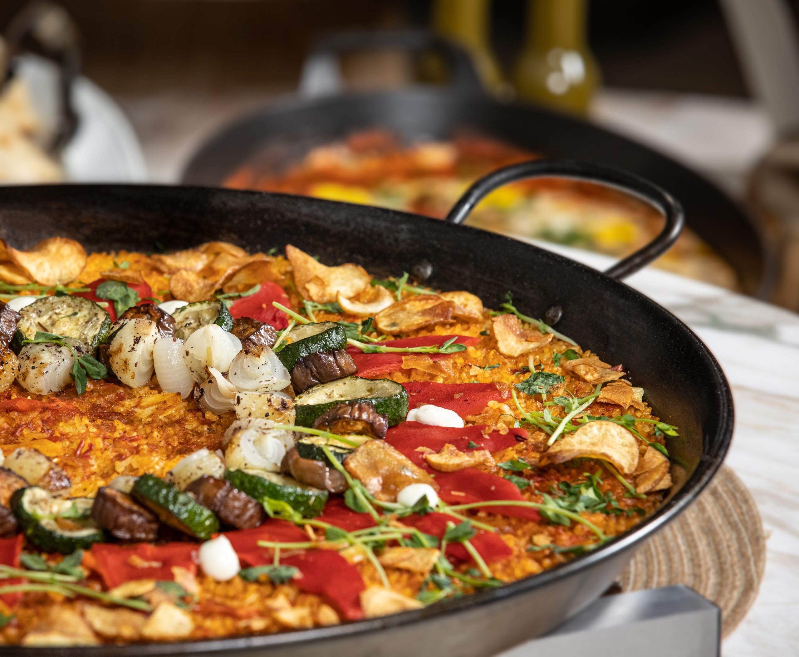 The close-up of a paella dish in a large black pan, with rice, seafood, peppers and meat.