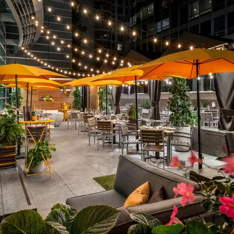 An outdoor terrace at night, with orange umbrellas, plants, string lights, a grey banquette and dining tables at Renoir, a restaurant in Montreal