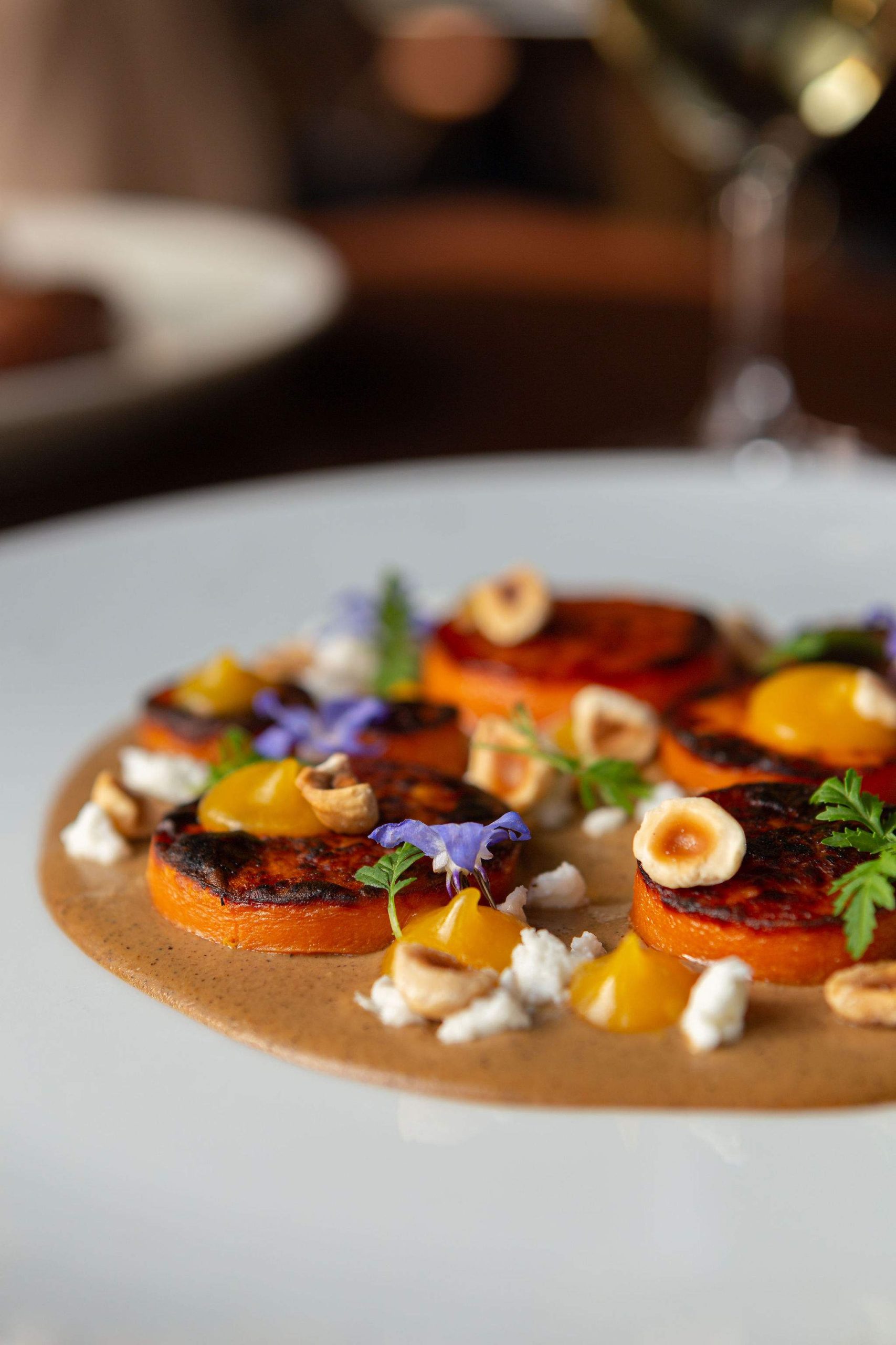 A close-up photo of a dish featuring slices of sweet potato on a brown sauce, with colourful flowers and herbs, at River Café, a restaurant in Calgary