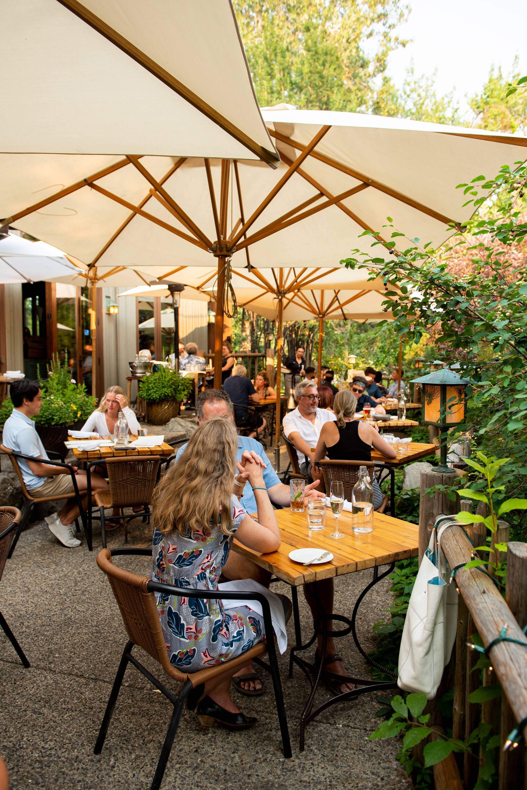 Customers dine on River Café’s patio in Calgary featuring off-white umbrellas and wooden tables and chairs.