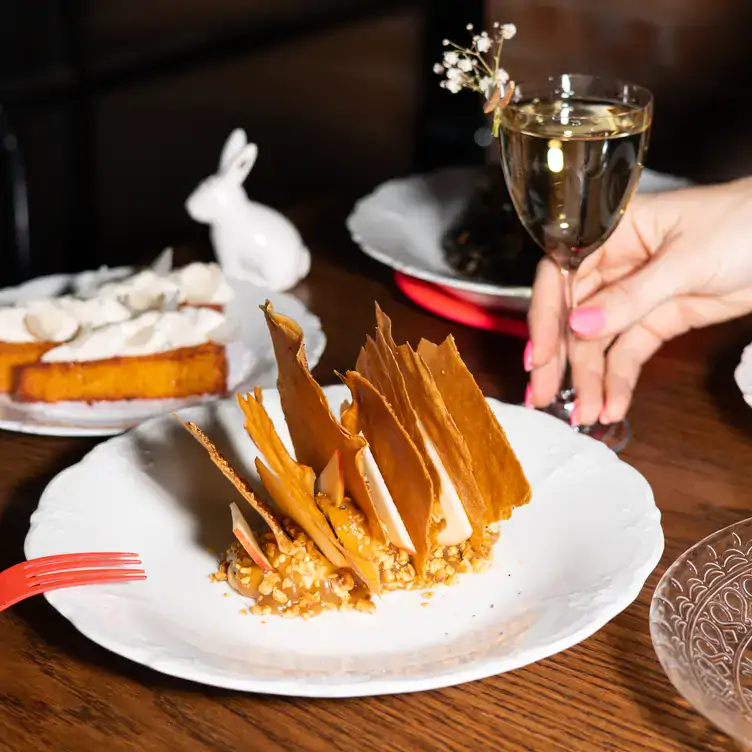 A hand grabs a glass of white wine topped with flowers neaxt to a crispy dish at Lapinou, one of the best French wine bars in Toronto