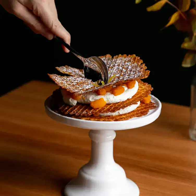 Un·e client·e tient une cuillère en argent et tranche un dessert composé de gaufrettes et de crème sur un socle à gâteau blanc chez Annette bar à vin, l'un des meilleurs restaurants de Montréal.