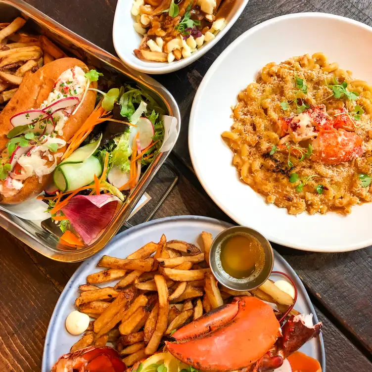 Des assiettes de fruits de mer comprenant un lobster roll, du crabe, des frites et des pâtes au Pincette Bar à Homard, l'un des meilleurs restaurants pour bruncher à Montréal.