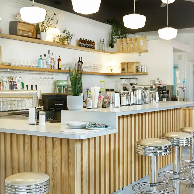 A bright and airy cafe with a bar, shelves and hanging lights at Mira Mira Diner, one of the best brunch spots in Toronto