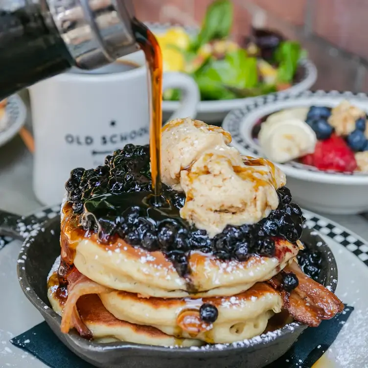 A stack of pancakes topped with blueberries, bacon, ice cream and maple syrup at Old School - Toronto