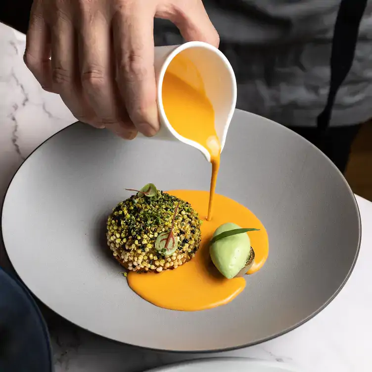 A waiter pours an orange sauce over a ball-shaped dish covered in pistachio crumbs at Boulevard Kitchen & Oyster Bar in Vancouver