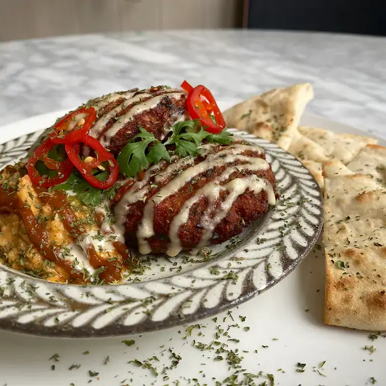 A Korean-inspired dish topped with white sauce and coriander sits next to pita bread at Té, a fusion restaurant in Toronto