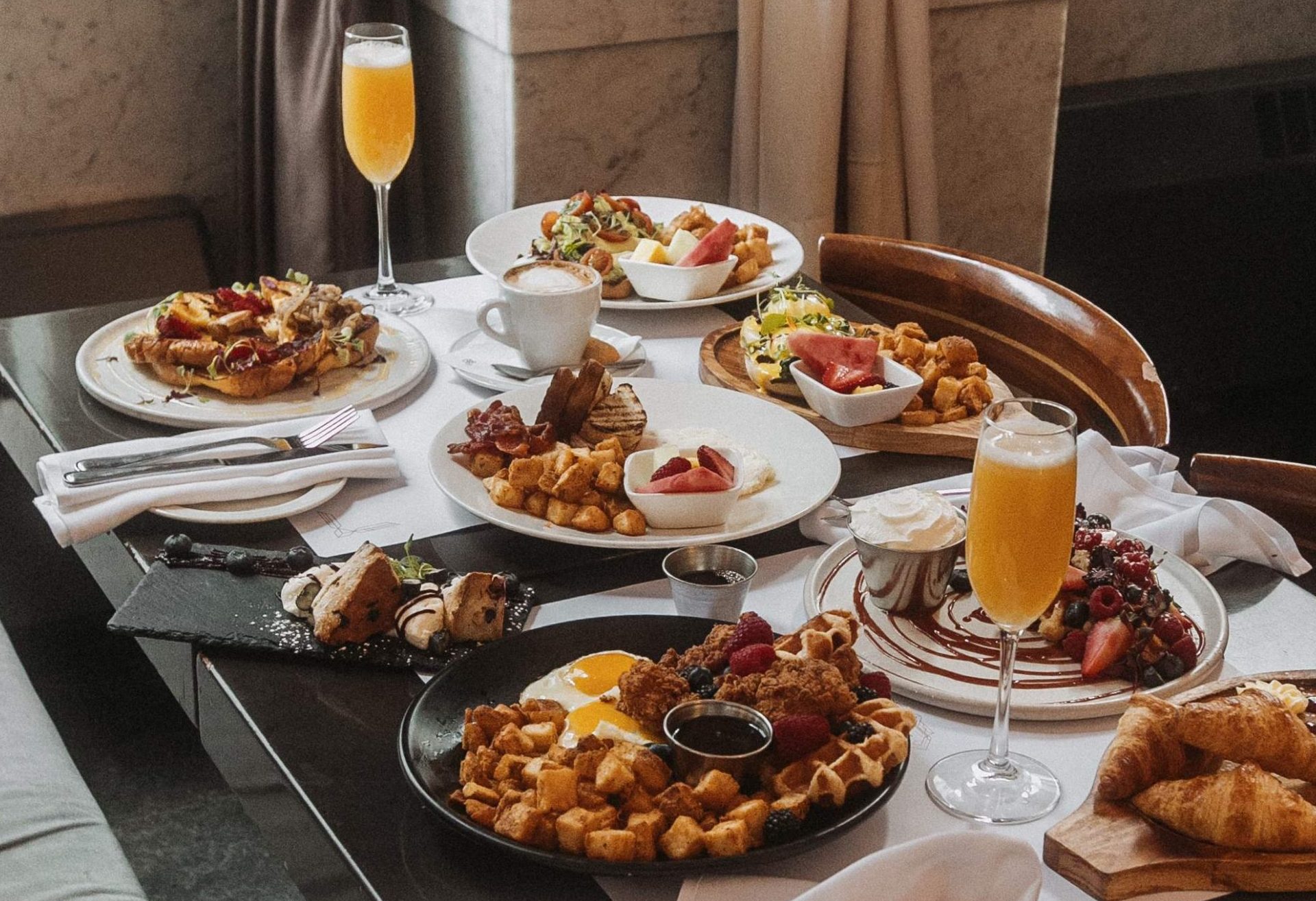 A spread of breakfast dishes featuring eggs, potatoes, pastries and mimosas at Brasserie 701