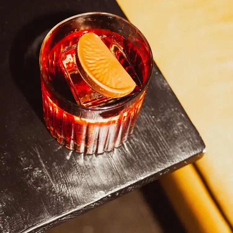 A red cocktail with a slice of orange on top, from the menu at Negroni Room, one of the best bars in Montreal.