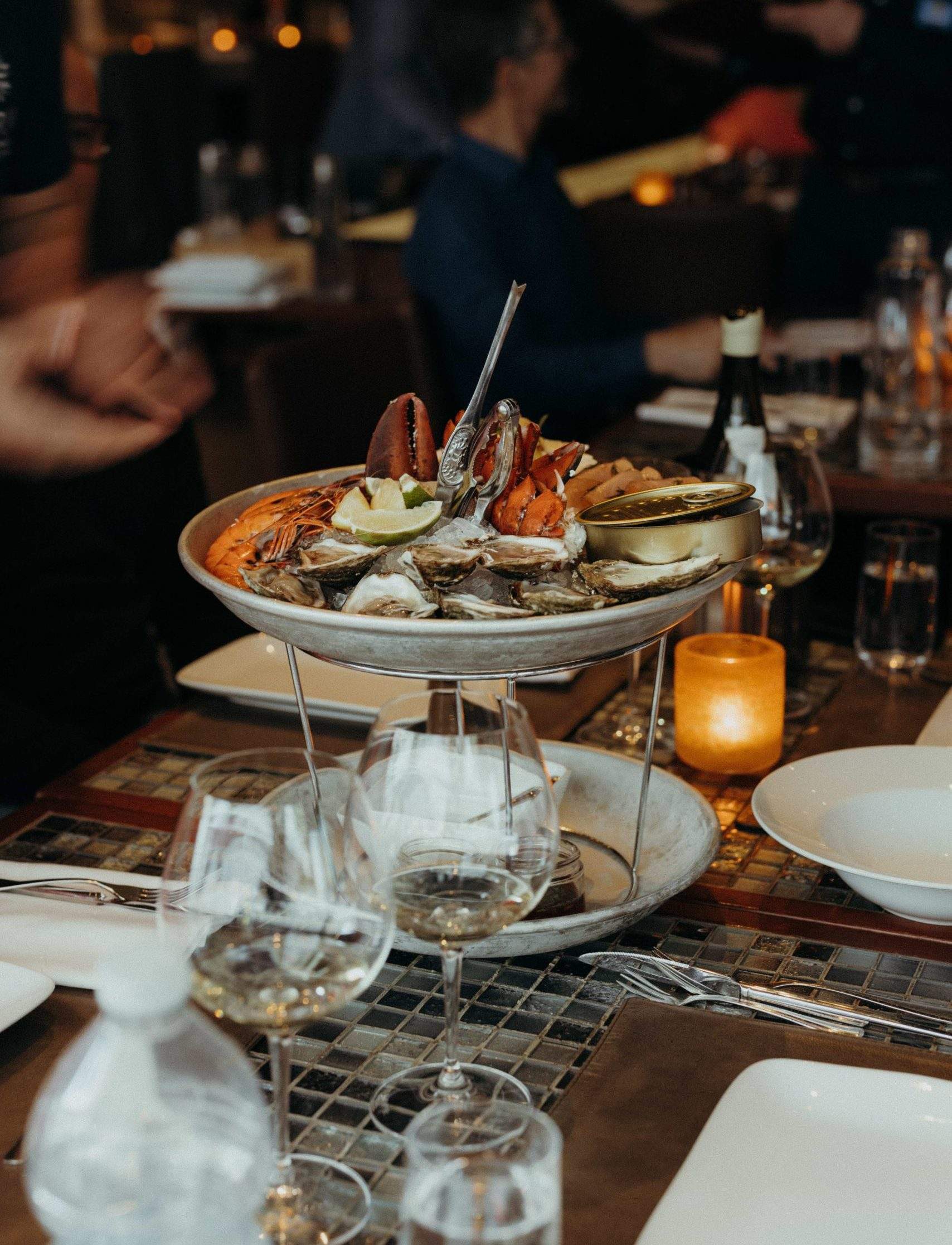 A two-tier plate of lobster, oysters, and other seafood on a tiled table at Montreal restaurant Ferreira Café.