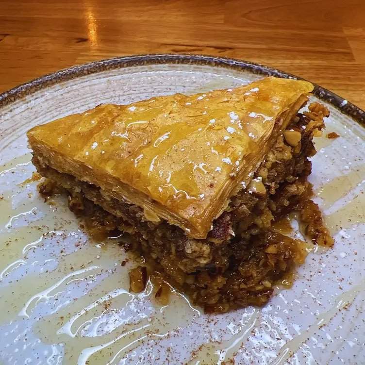 Un morceau de baklava arrosé de miel servi sur une assiette en céramique artisanale chez Tzatzi-qui, un des meilleurs nouveaux restaurants de 2023 à Montréal.