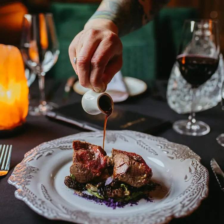 A dark sauce is drizzled over a meat course at Calgary restaurant Sauvage.