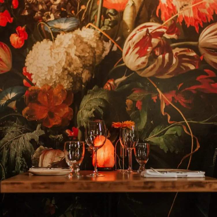 A wooden table topped with wine glasses with a colourful floral mural on the wall at Calgary restaurant Sauvage.