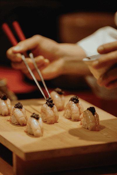 Une personne dépose de la garniture sur des sashimis déposés sur un plateau de service en bois au restaurant Okeya Kyujiro à Montréal