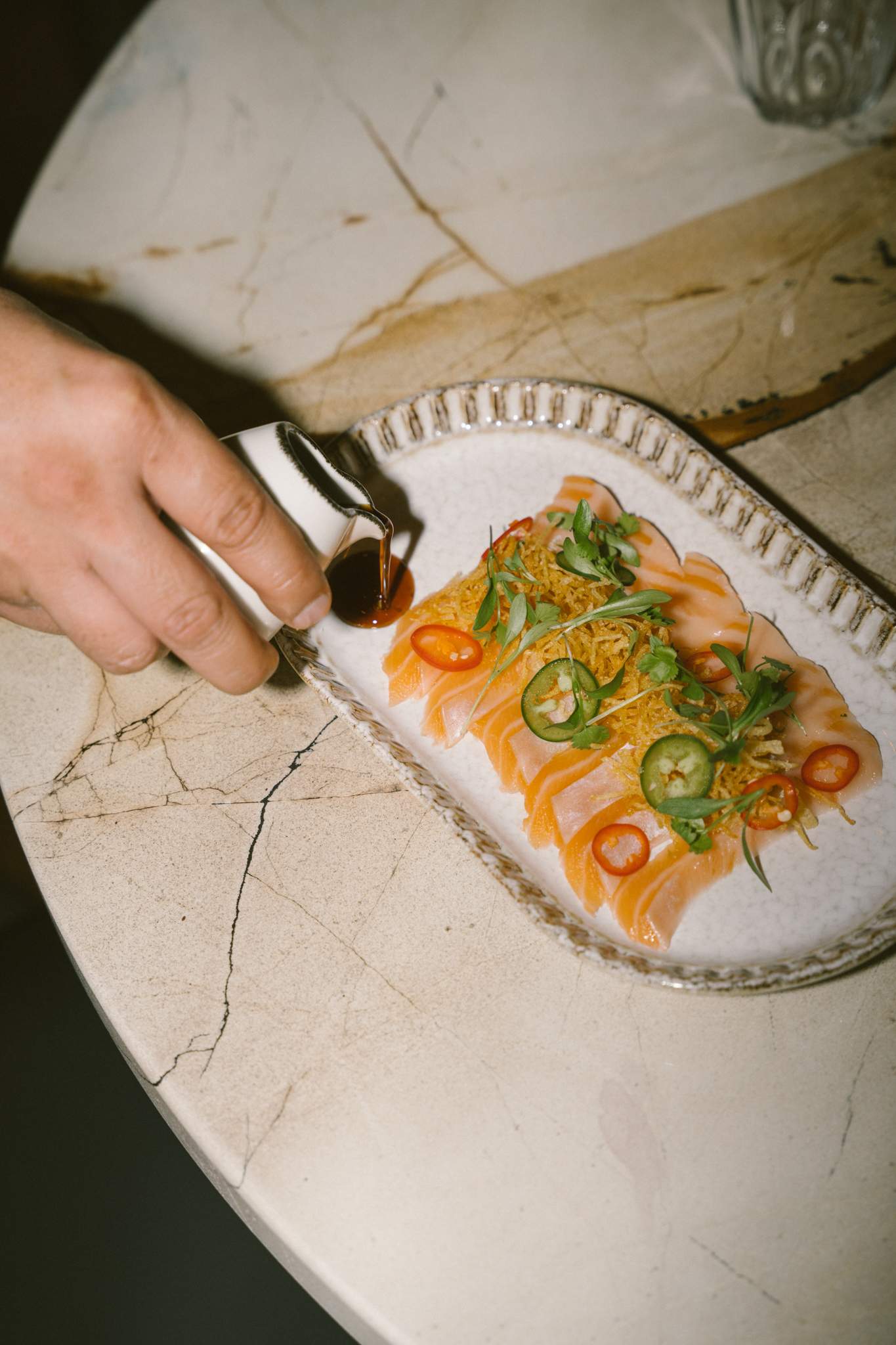 Une main verse une petite carafe de sauce sur un plat de ceviche surmonté de minces tranches de piments verts au Sabrosa, un des meilleurs nouveaux restaurants de 2023 à Montréal.