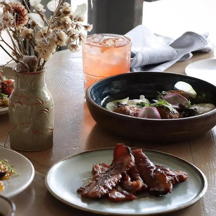 Bowls and plates of food, accompanied by floral arrangements at Farmer’s Apprentice, one of the best special occasions restaurants in Vancouver.