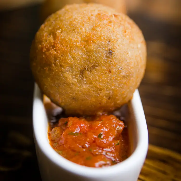 Un arancini à la joue de bœuf et champignon sur une coupelle de sauce tomate persillée et avec du parmesan de chez Il Bazzali