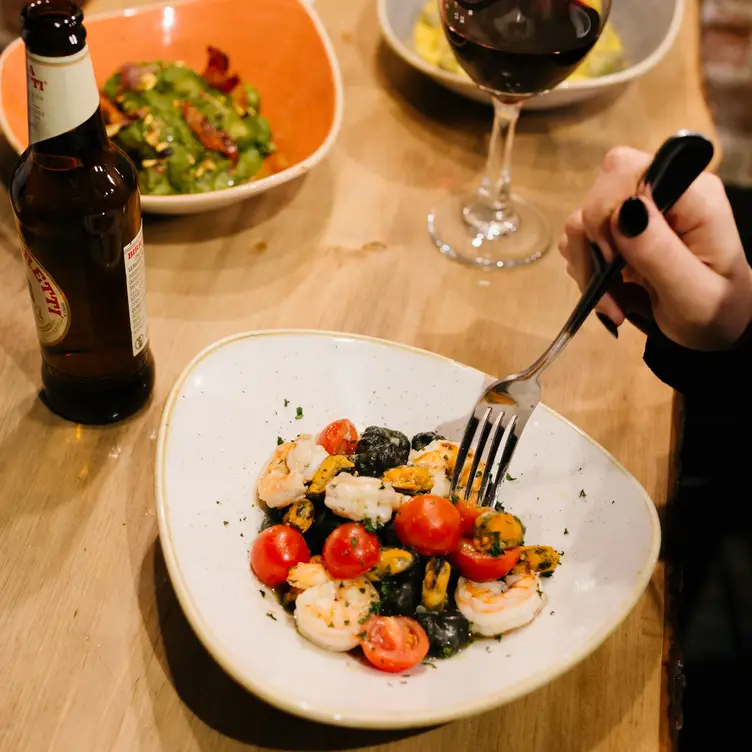 A salad with shrimp and tomatoes next to a glass of red wine at Tav Gnocchi & Pizza Bar, one of the best authentic Italian restaurants in Toronto.