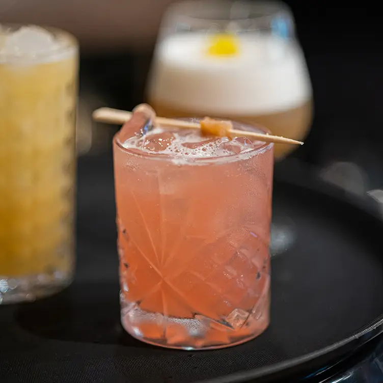 Un verre de cocktail avec une décoration à l’orange devant deux autres verres de cocktails de chez Bloom Sushi, l’un des meilleurs restaurants végans de Montréal.