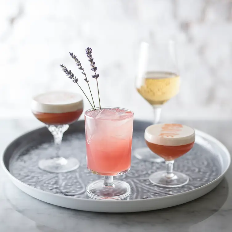 Deux verres de cocktail orange, une flûte de mousseux, un verre de cocktail rose avec de la lavande dedans, sur un plateau argenté de chez LOV McGill, l’un des meilleurs restaurants végans de Montréal.