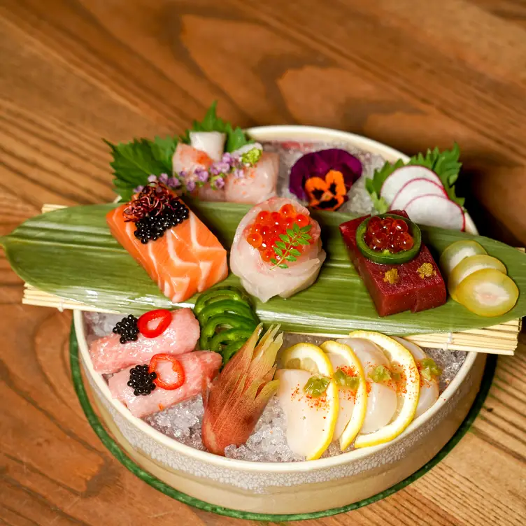 Un plat avec de la glace, des morceaux de poisson, une feuille de bambou, des fleurs et du rogue de chez Yoko Luna.