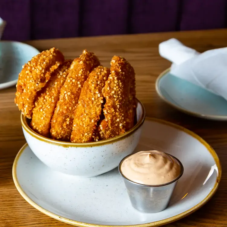 A bowl of fried quinoa onion rings placed on a plate with a cup of orange sauce from Fresh, one of the best family restaurants in Toronto.