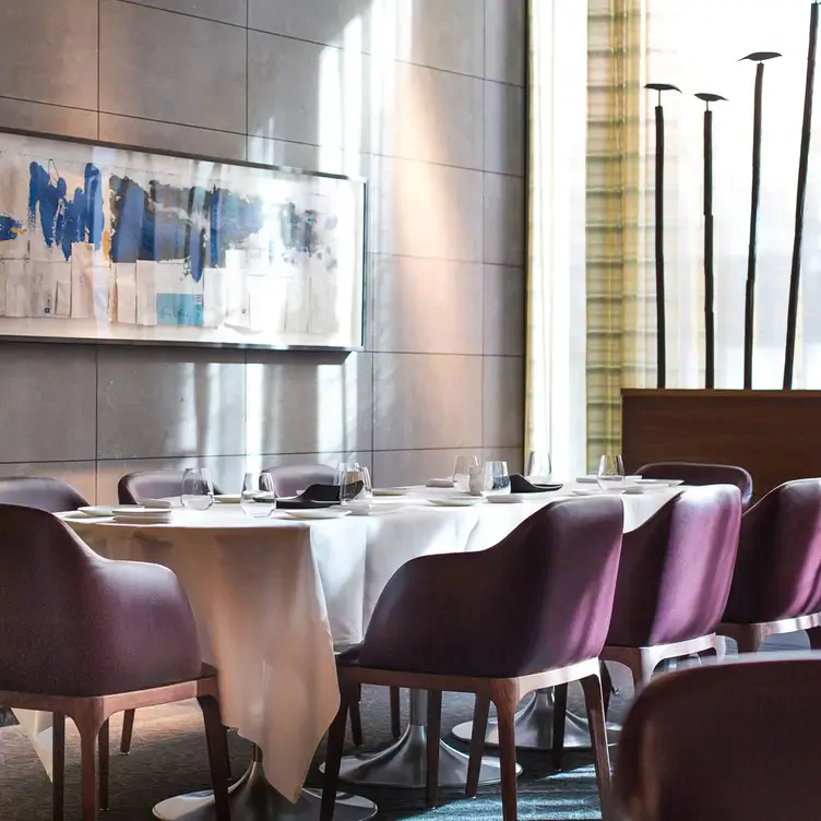 Une rangée de tables avec une nappe blanche, des fauteuils, des verres et des assiettes devant une peinture abstraite chez Restaurant Toque !, l’un des meilleurs restaurants français à Montréal.