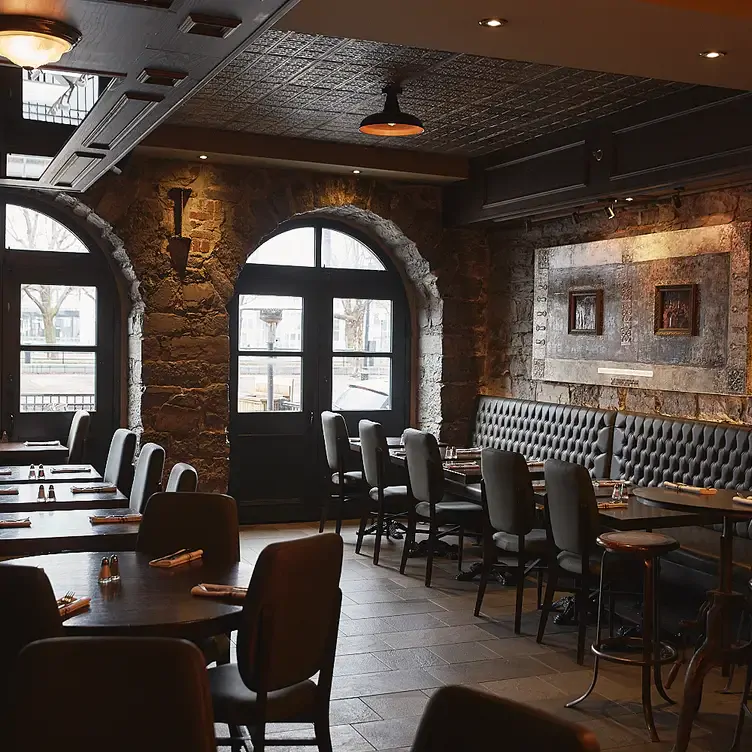 Deux rangées de tables avec des banquettes à côté d’un cadre avec deux peintures de chez Gaspar French Brasserie, l’un des meilleurs restaurants français à Montréal.