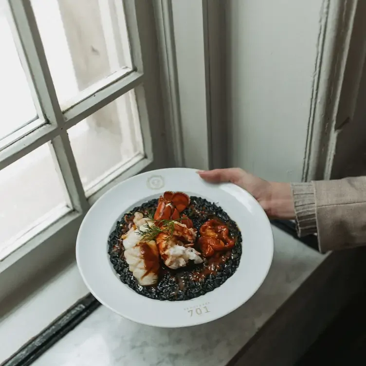 Une main tenant une assiette avec des morceaux de homard au sabayon de chez Brasserie 701, l’un des meilleurs restaurants français à Montréal.