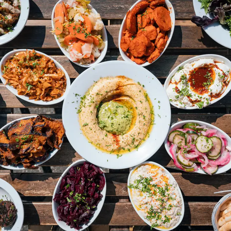 A dish of hummus in the centre of eight bowls of dips at Chickpea in Vancouver.