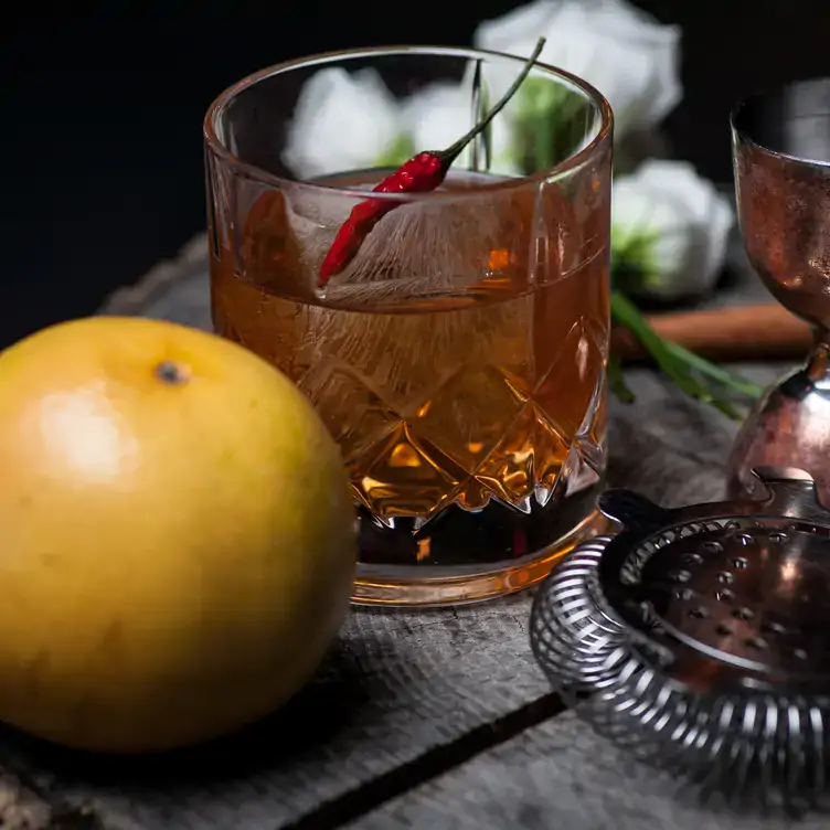 A classic cocktail garnished with a chili pepper and surrounded by bar utensils from Belmont.