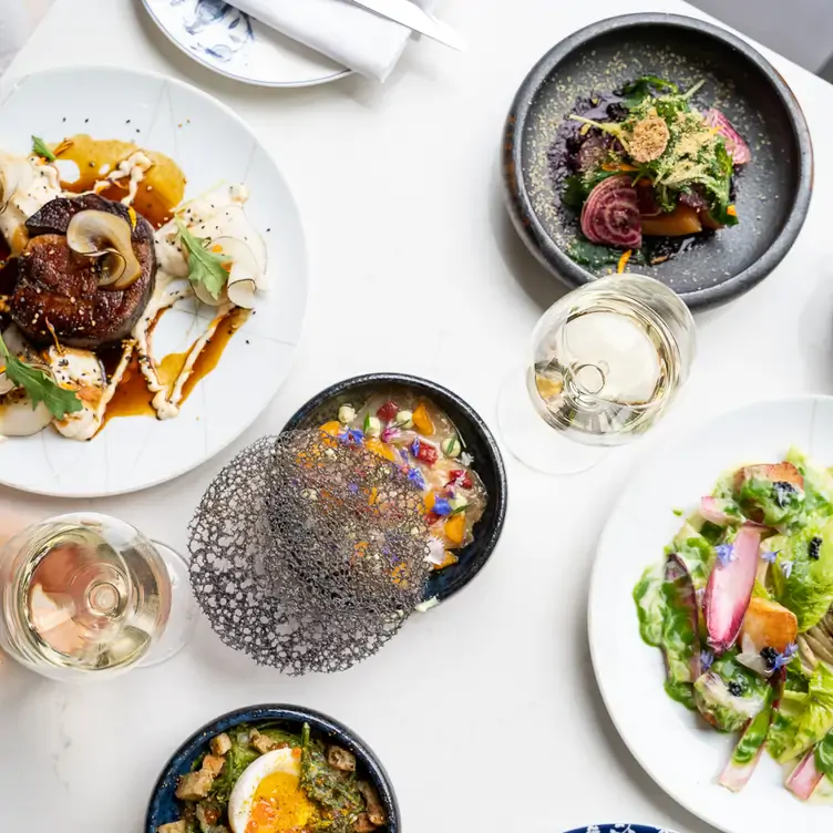 Une table garnie de plusieurs assiettes avec des aliments colorés et un verre de vin blanc de chez Rosélys, l’un des meilleurs restaurants familiaux de Montréal.