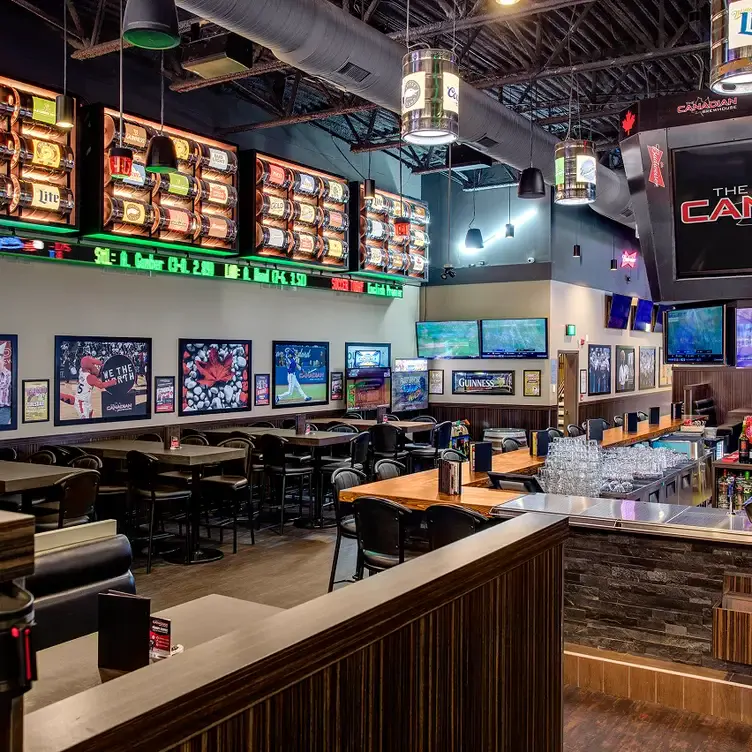 A restaurant with several tables, a large bar, and a wall with numerous television screens and sports decorations from The Canadian Brewhouse, one of the best family restaurants in Edmonton.