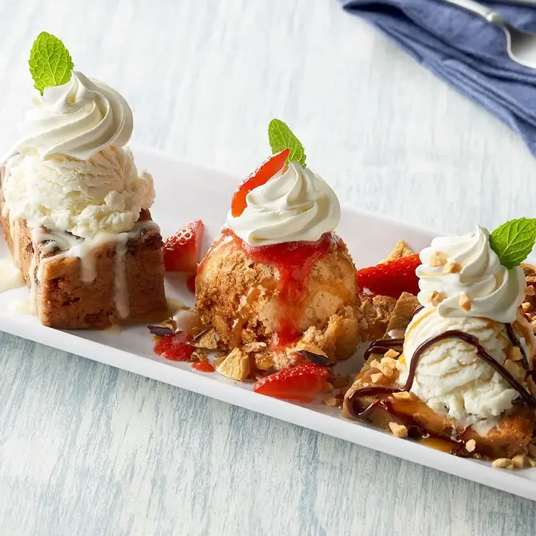 A plate with two cakes topped with ice cream and whipped cream, and a scoop of ice cream with whipped cream, mint, and strawberry slices from Bubba Gump, one of the best family restaurants in Edmonton.