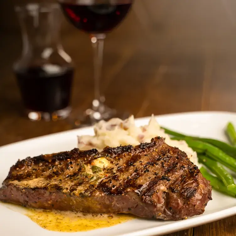 A plate with a piece of beef covered in spices, accompanied by mashed potatoes and green beans from Mr Mikes SteakhouseCasual, one of the best family restaurants in Edmonton.