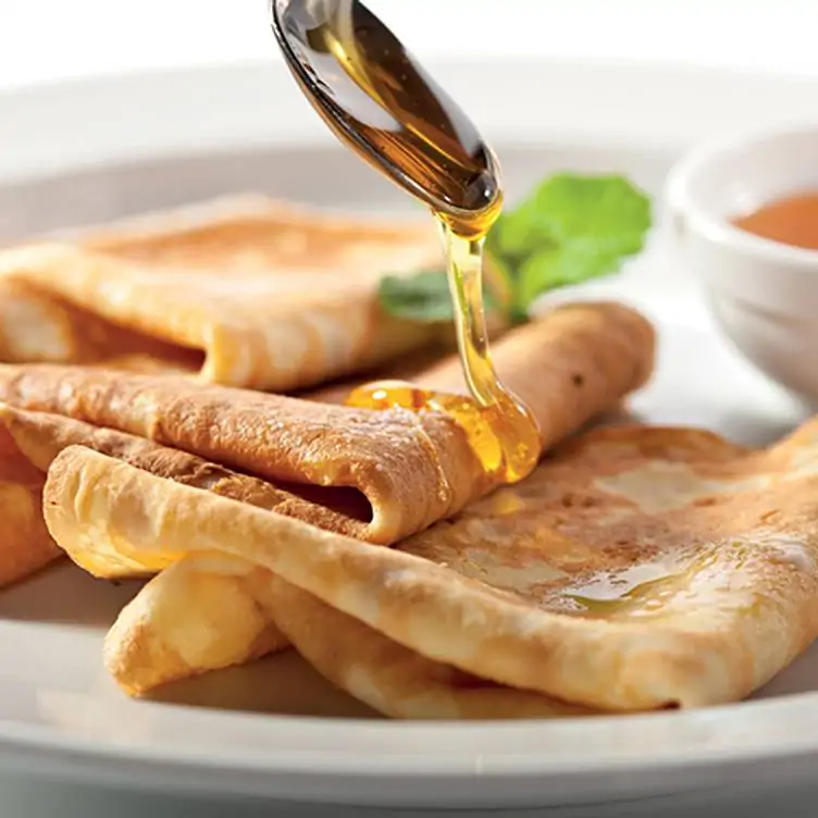 A spoon pouring honey over a stack of crêpes from Arôme, one of the best brunch spots in Ottawa.