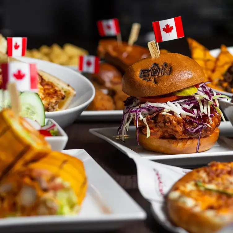 A variety of dishes each topped with a small Canadian flag, including a burger with coleslaw and a large piece of meat from The Canadian Brewhouse, one of the best family restaurants in Edmonton.