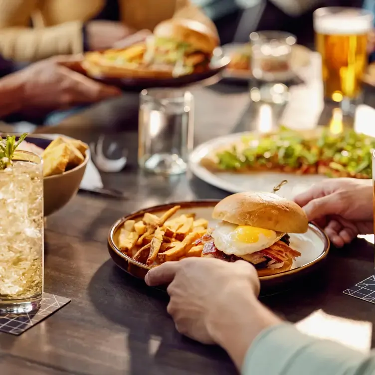 A plate with a bacon and egg burger accompanied by fries and a glass of refreshing beverage at The Rec Room, one of the best family restaurants in Edmonton.